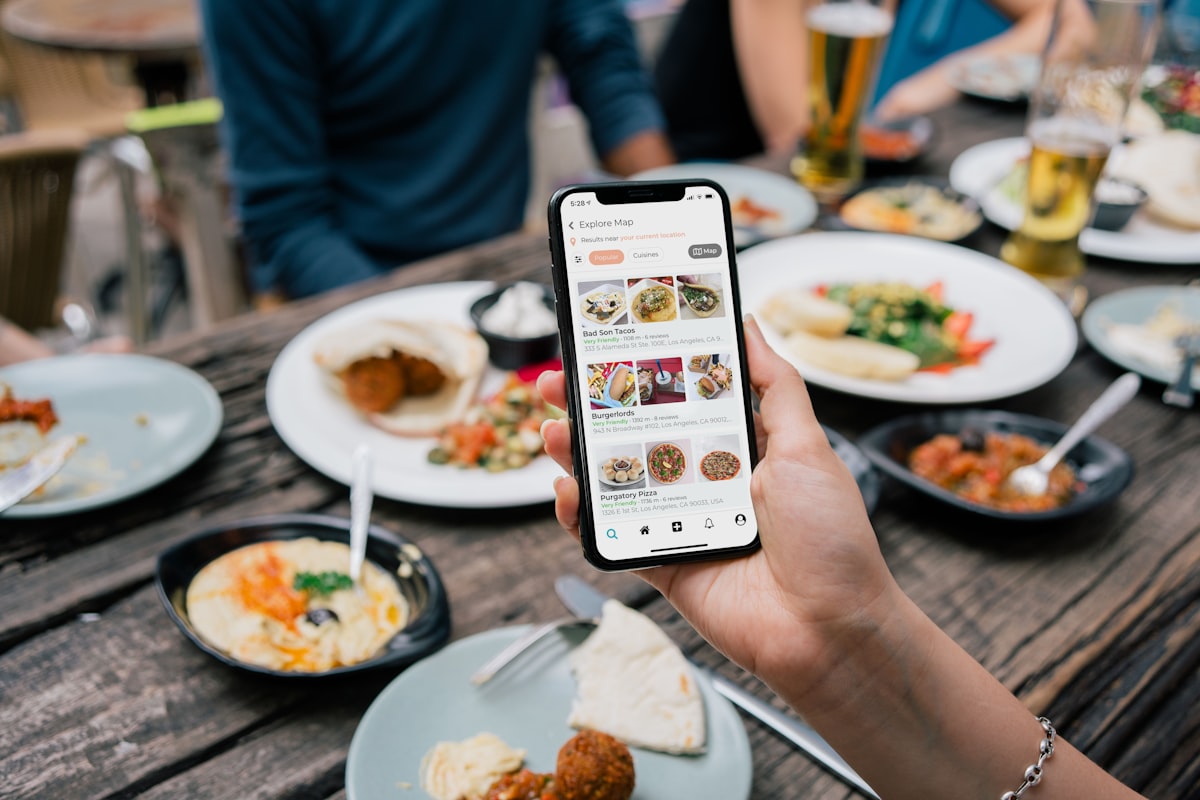 料理の並ぶテーブルでスマートフォンの飲食店アプリを使う人
